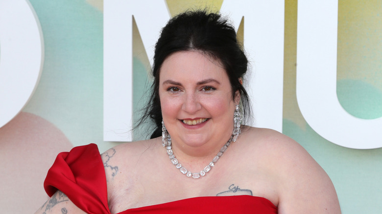 Photo en gros plan de Lena Dunham souriant sur le tapis rouge, dans une robe rouge