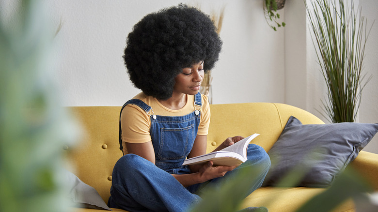 Une femme est assise sur un canapé et lit un livre