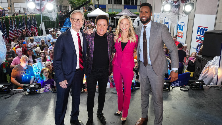 Ainsley Earhardt dans un pantalon Fuschia posant avec Donny Osmond