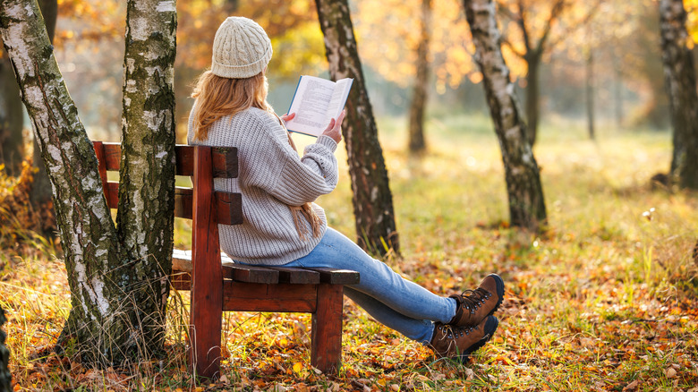 Une femme lisant sur un banc entouré d'arbres