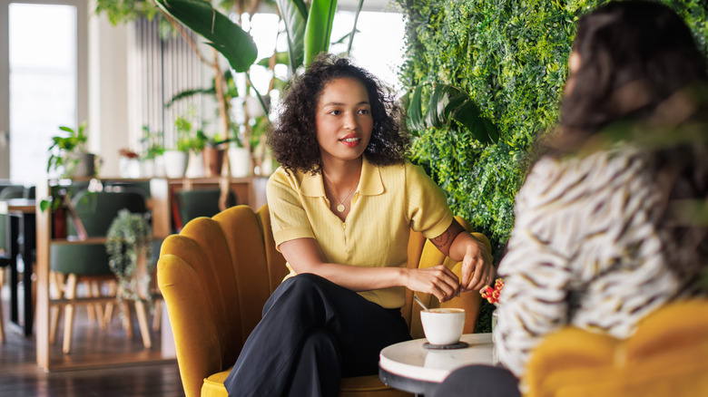 Deux femmes assises sur des chaises dans un café rempli de plantes et se sont engagées dans la conversation