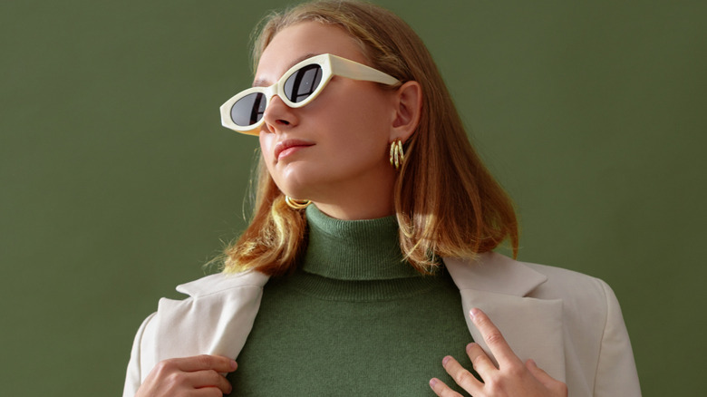 Femme portant des lunettes de soleil blanches, un col roulé vert et un costume beige