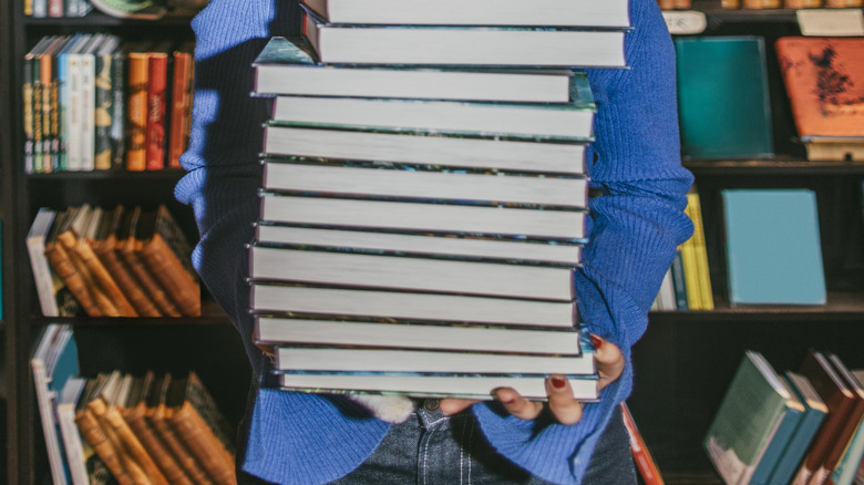 Femme furtivement une grande pile de livres