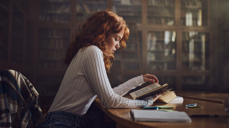 Une femme aux cheveux rouges lisant dans une bibliothèque