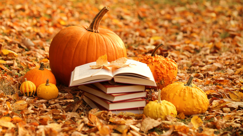 Livre ouvert placé au sommet d'une pile de livres et entouré de feuilles d'automne et de citrouilles