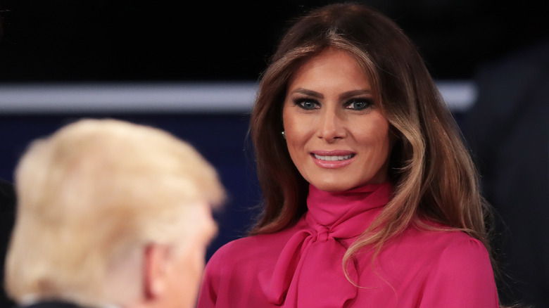 Melania Trump dans une blouse rose souriant à Donald Trump lors d'un débat en 2016