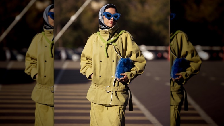 Une femme avec une tenue vert olive et des accessoires bleus photographiée à l'extérieur