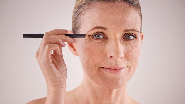 Une femme s'applique un eye-liner avec un crayon marron