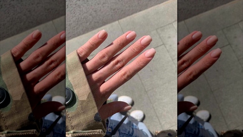 Une main avec des ongles beiges dans un style court et carré arrondi