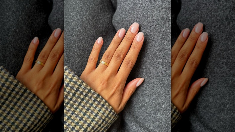 Une main avec des ongles roses aux pointes carrées et arrondies et une bague en or