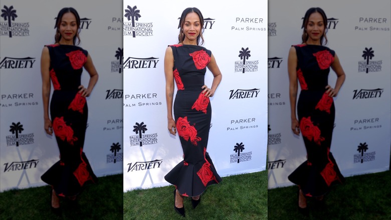 Zoe Saldana posant avec une main sur la hanche tout en portant une robe noire moulante avec une jupe évasée