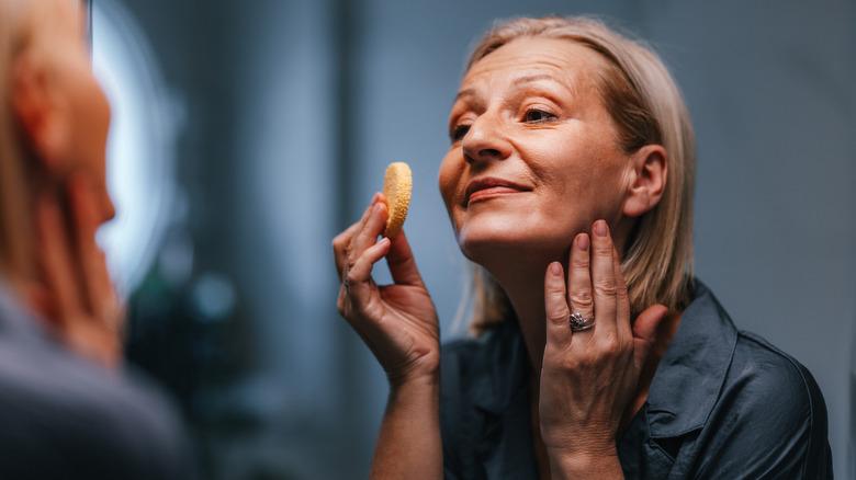 Une femme se maquillant le visage dans le miroir avec une éponge