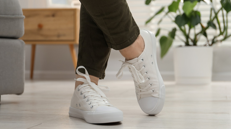 Personne portant des baskets blanches debout sur un parquet clair