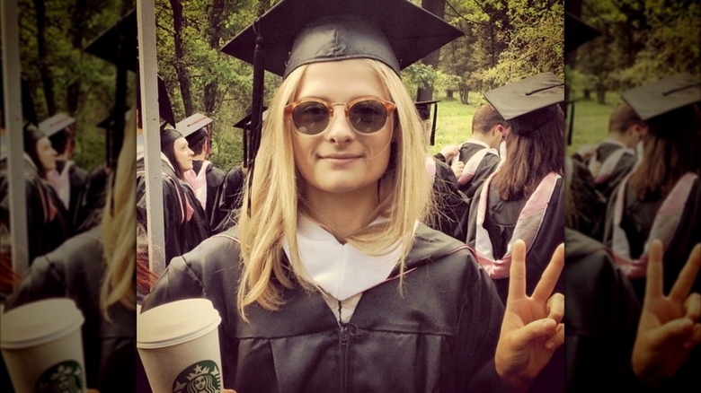 Louisa Jacobson portant une toge et un chapeau de remise des diplômes tout en jetant un signe de paix et en tenant une tasse Starbucks