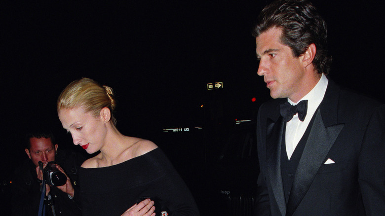 John F. Kennedy Jr. et Carolyn Bessette marchant ensemble, un photographe essayant de prendre une photo avec un appareil photo en arrière-plan