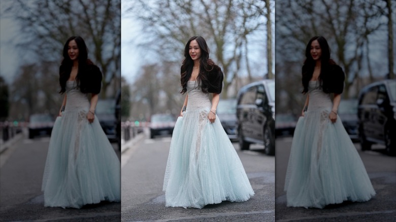 Une femme vêtue d'une robe transparente bleu clair avec un bolo en fourrure noire, dans une rue de la ville