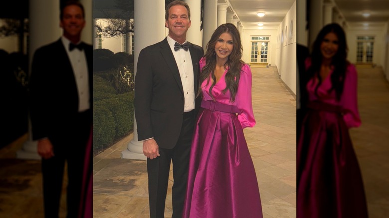 Kristi Noem dans une robe rose debout à côté de son mari Bryon Noem dans un couloir extérieur de la Maison Blanche