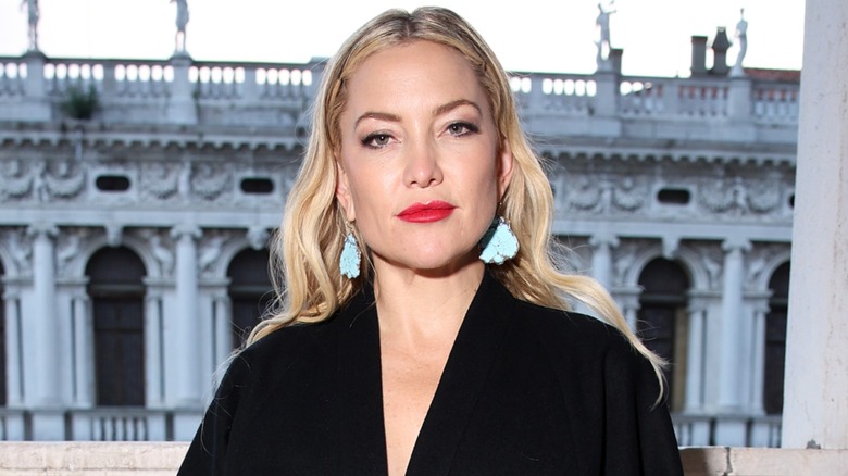Kate Hudson posant devant un vieux bâtiment et portant du rouge à lèvres