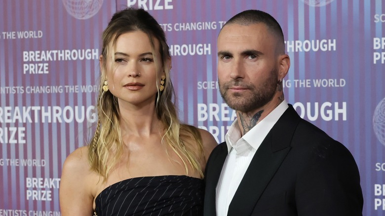 Behati Prinsloo posant avec une expression neutre à côté d'Adam Levine sur le tapis rouge