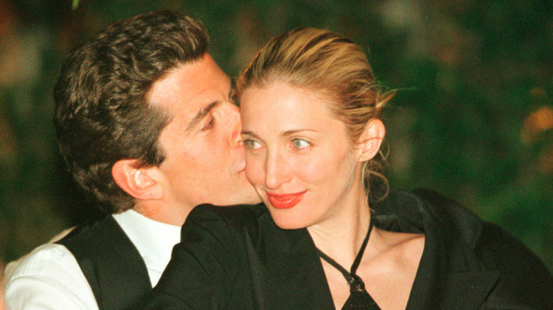 John F. Kennedy Jr. assis derrière Carolyn Bessette-Kennedy et l'embrassant sur la joue
