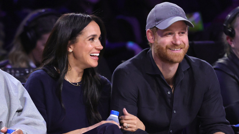 Le prince Harry et Meghan Markle sourient et sont assis au bord du terrain lors d'un match