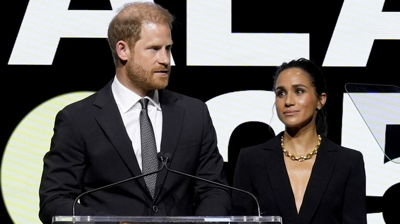 Le prince Harry et Meghan Markle sur un podium et vêtus de noir