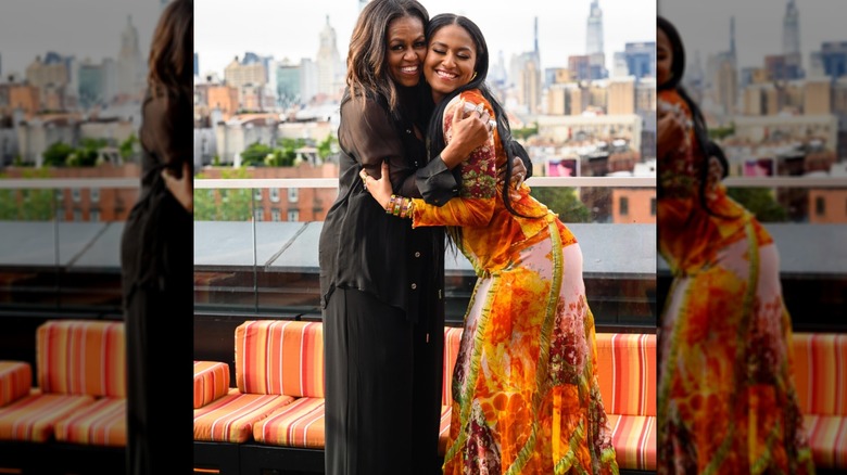 Michelle Obama porte une tenue entièrement noire tout en serrant Sasha Obama dans une robe longue orange.