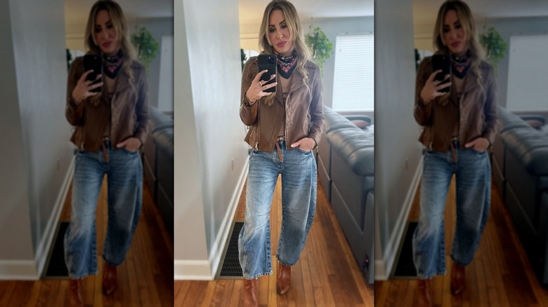 Une femme portant un jean tonneau et des bottines, posant pour un selfie devant un canapé noir