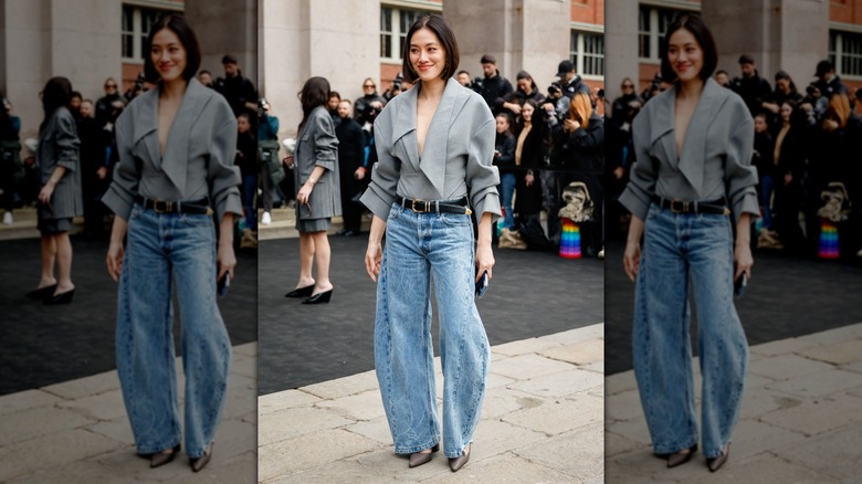 Une femme debout dehors, portant un jean tonneau avec une chemise grise et des mules