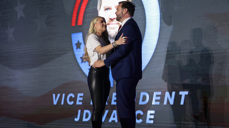 Erika Kirk, en pantalon moulant en cuir noir, et JD Vance, en costume bleu marine, s'embrassent sur scène.