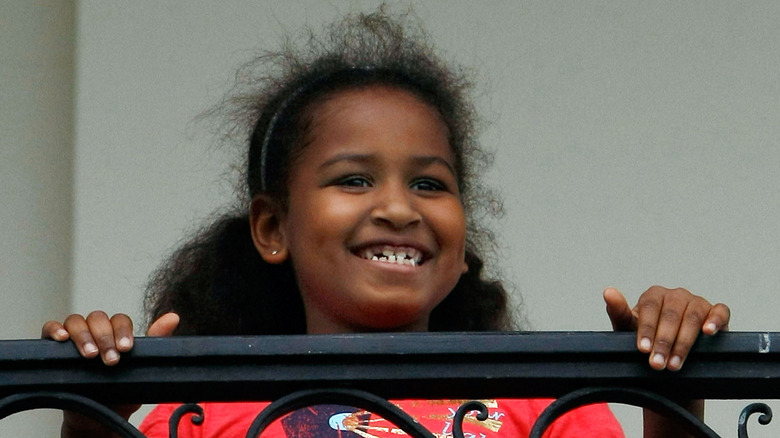 Sasha Obama sourit en se tenant à la balustrade d'un balcon