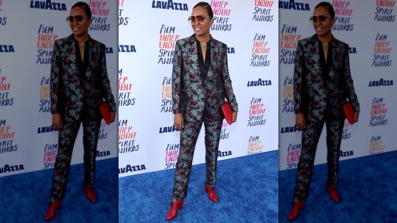 Aisha Tyler portant un costume à motifs, de grosses lunettes de soleil et des bottes à talons lors d'un événement en 2024