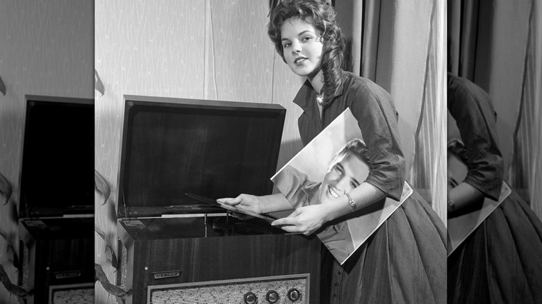 Priscilla Presley tenant un vinyle d'Elvis Presley regardant la caméra