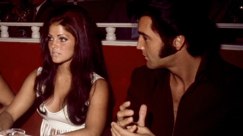 Priscilla Presley aux longs cheveux roux est assise à côté d'Elvis Presley aux favoris noirs
