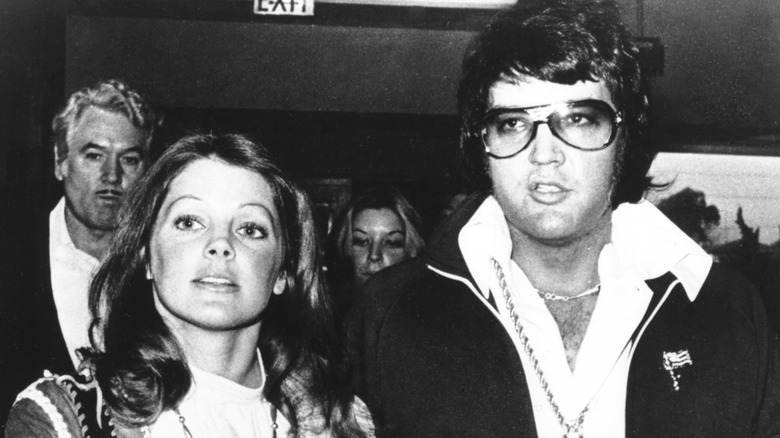 Priscilla Presley tient la main d'Elvis Presley qui porte des lunettes