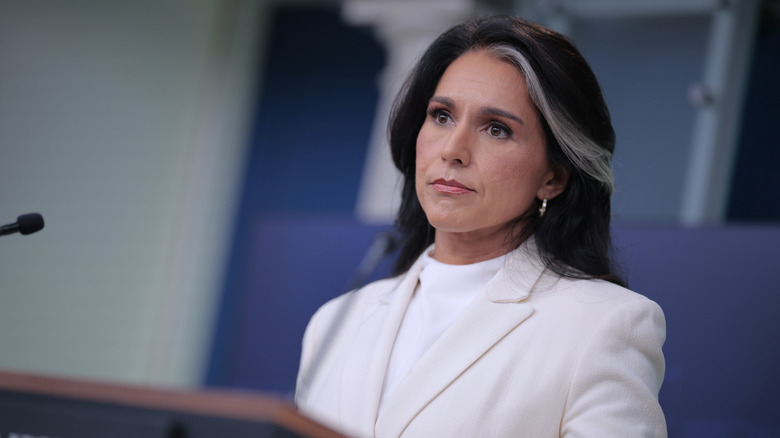 Tulsi Gabbard portant un costume blanc debout sur un podium et fronçant les sourcils