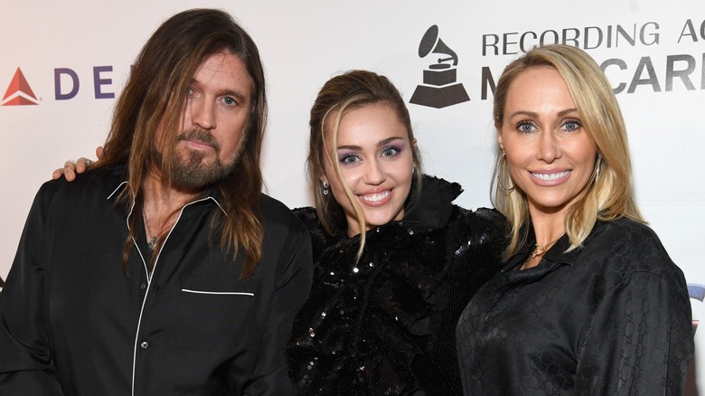Billy Ray Cyrus, Miley Cyrus et Tish Cyrus posant ensemble sur le tapis rouge devant un fond blanc