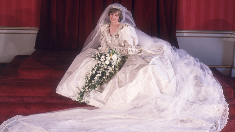 La princesse Diana est assise dans sa volumineuse robe de mariée et tient des fleurs.