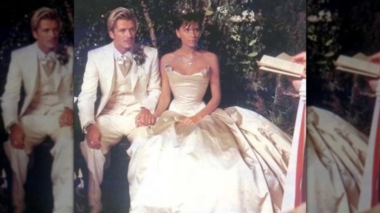 Victoria Beckham est assise à côté de David Beckham, vêtue d'une robe de mariée en satin.