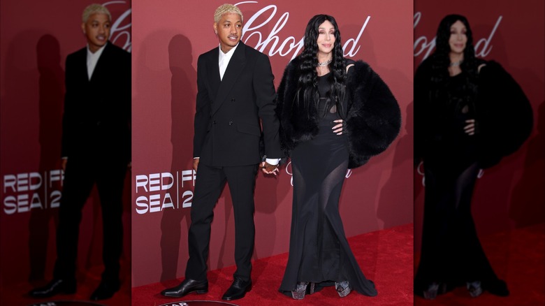 Cher aux côtés d'Alexander Edwards, vêtue d'une robe transparente noire et d'un manteau de fourrure noir.