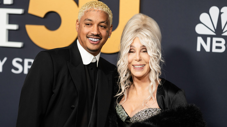 Cher sourit avec des cheveux blancs, à côté d'Alexander Edwards avec des cheveux blonds