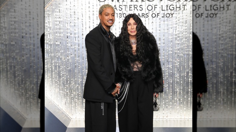 Cher aux côtés d'Alexander Edwards portant un haut transparent et un manteau de fourrure noir