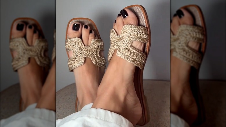 Une femme portant des claquettes en raphia avec du vernis à ongles foncé sur les orteils