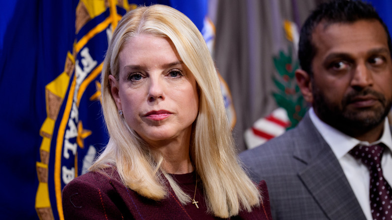 Pam Bondi avec les cheveux mi-longs regardant la caméra avec Kash Patel derrière elle