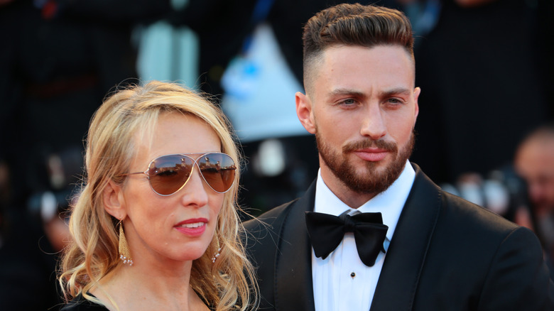 Sam Taylor-Johnson sourit avec des lunettes de soleil à côté d'Aaron Taylor-Johnson en costume