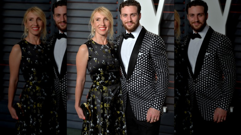 Sam Taylor-Johnson sourit dans une robe longue à fleurs à côté d'Aaron Taylor-Johnson dans un blazer psychédélique gris et noir
