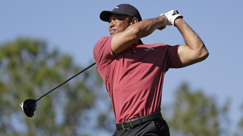 Tiger Woods balançant un club de golf portant une chemise rayée rouge et blanche et une casquette de baseball noire