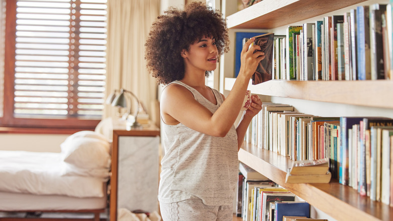 Femme tenant une tasse et lisant le dos d’un livre devant une grande bibliothèque