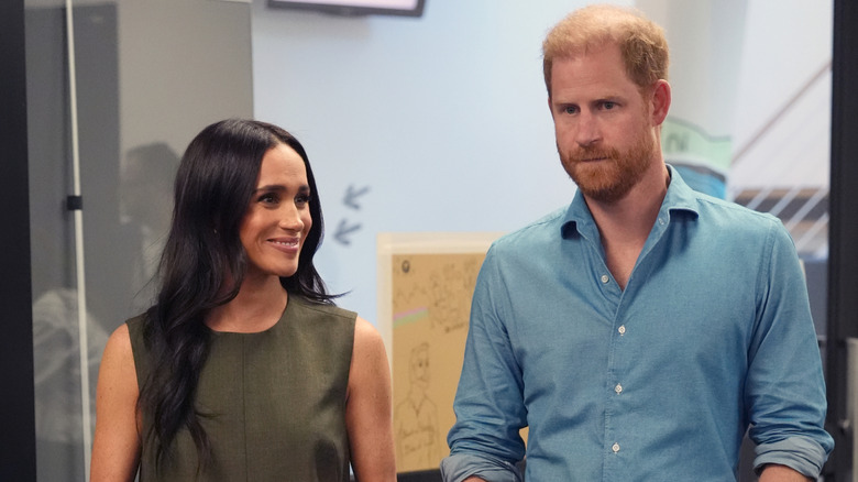 Le prince Harry et Meghan Markle lors d'un événement, avec Meghan souriant et Harry semblant neutre