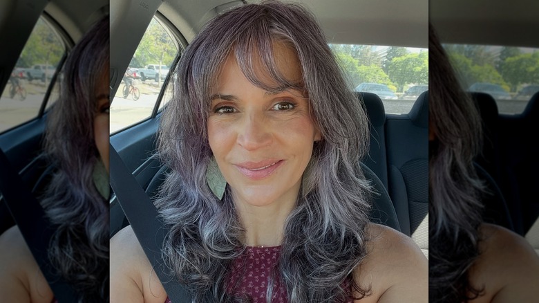 Une femme posant dans une voiture avec une coupe de cheveux courte, grise et violette